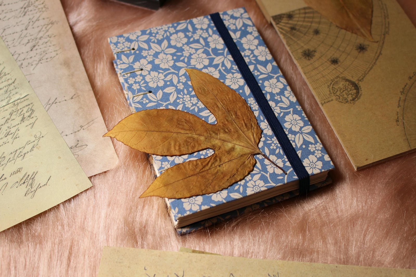 A flat lay of a vintage-themed journaling setup featuring a floral notebook and dried leaves.