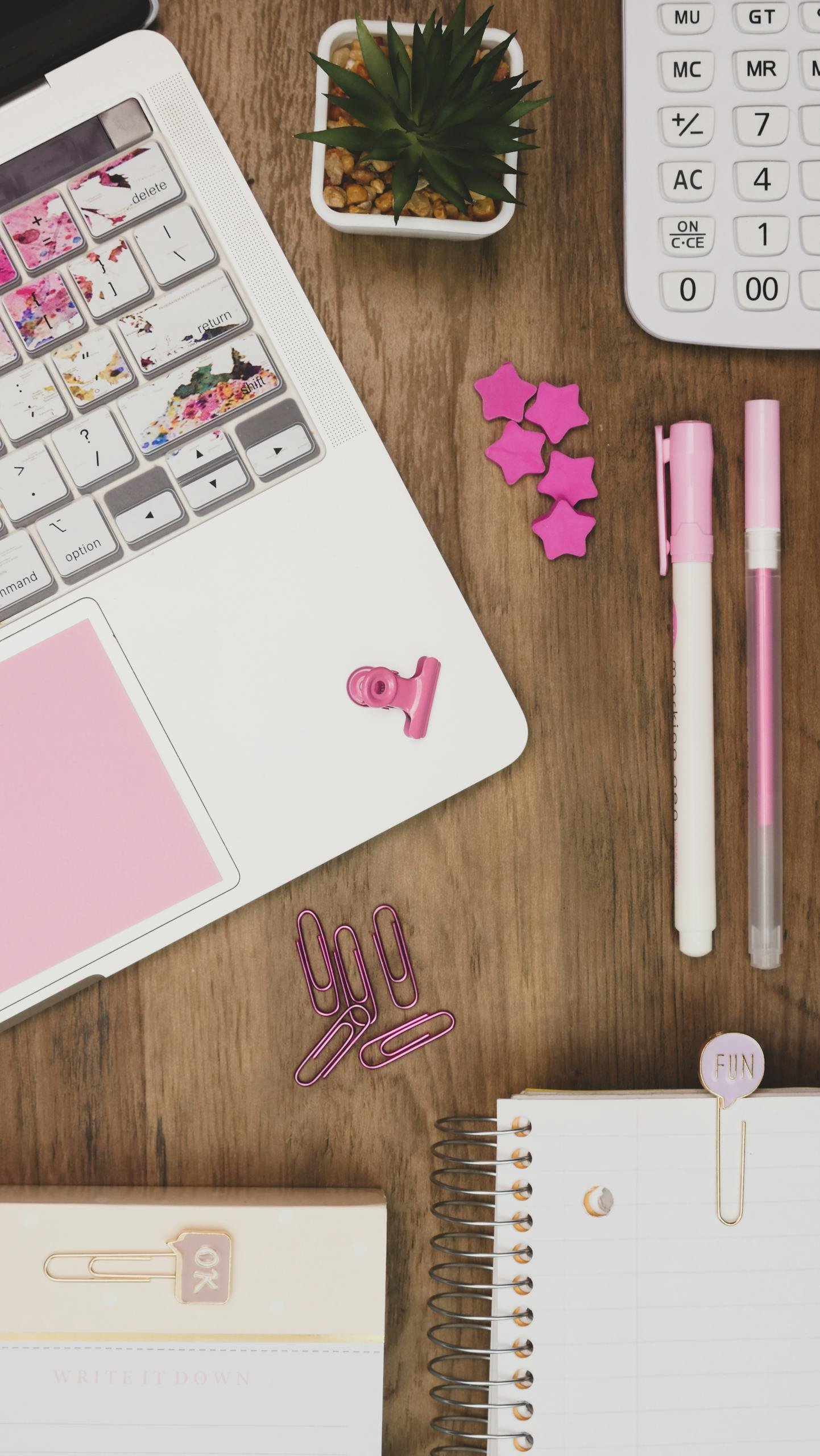 Overhead view of a stylish workspace featuring pink office supplies on a wooden desk.