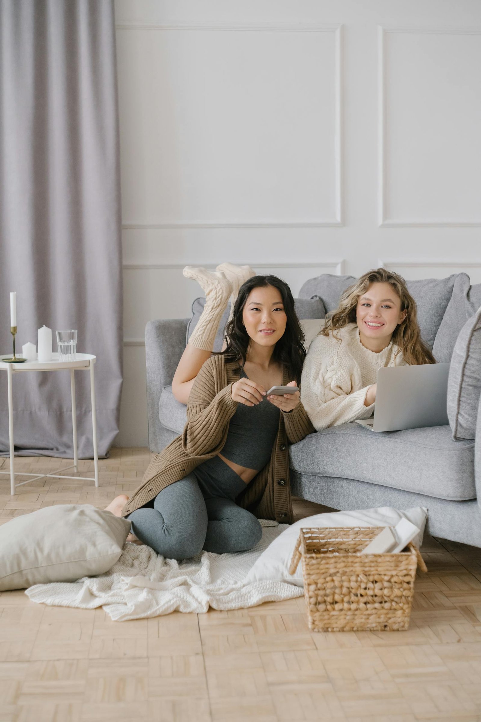 Two friends relaxing at home using a laptop and smartphone, showcasing comfort and connectivity indoors.